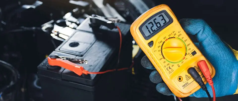 Mechanic checking car battery voltage with digital multimeter